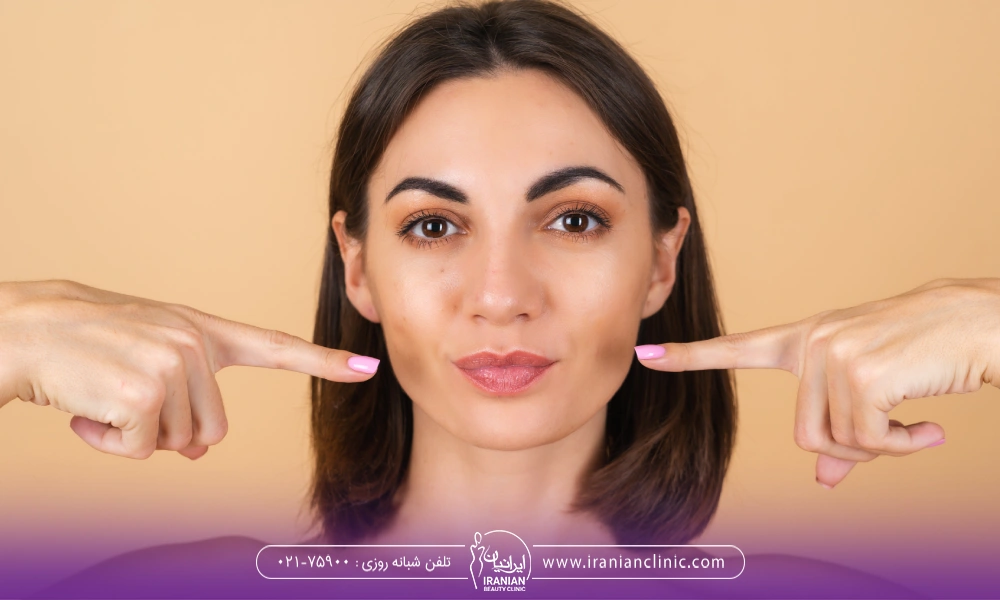 خانمی با موهای مشکی که به گونه هایش اشاره میکند
