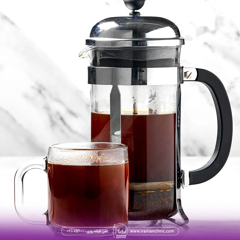 یک فنجان قهوه در کنار فرنچ پرس که داخل آن قهوه ریخته شده است