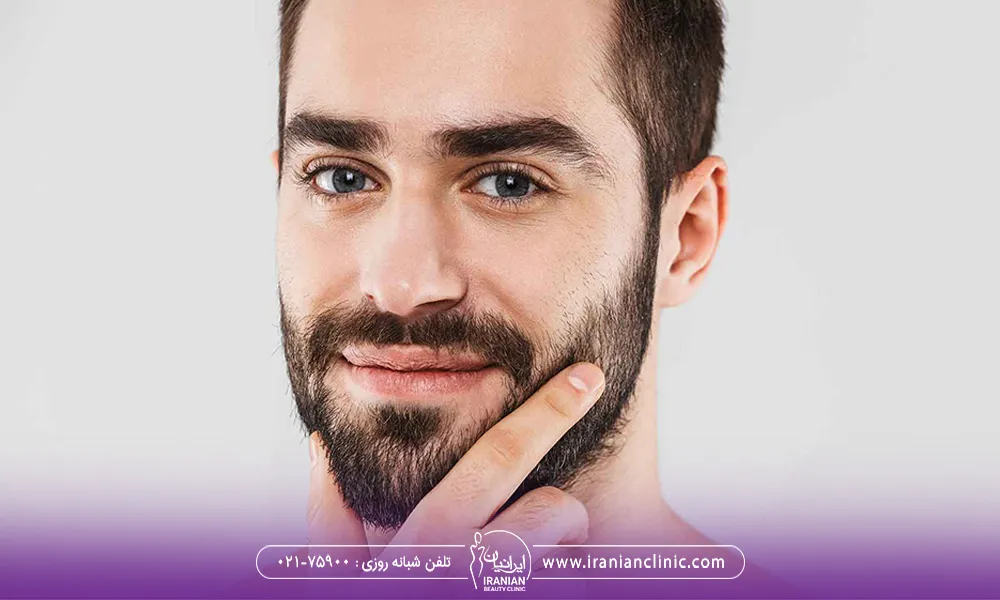 یک آقای چشم رنگی که با دستش به ریش صورتش اشاره می کند