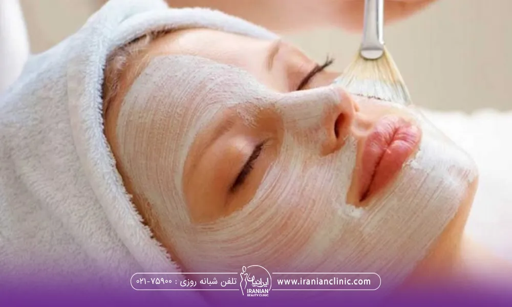 خانمی که حوله دور سرش پیچیده است و در حال گذاشتن مواد فشیال با قلمو روی صورتش است